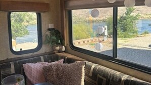 Interior acogedor de una autocaravana con zona de asientos acolchada, una ventana con vista a un lago y una lámpara colgante.