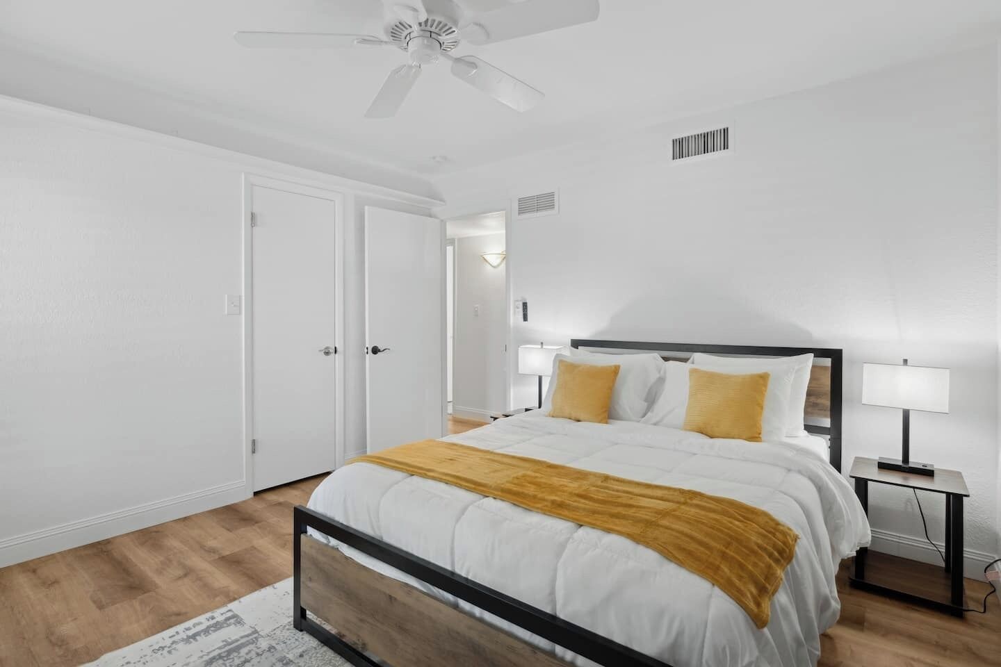 A bedroom with a bed, bedside tables, a ceiling fan, and white walls.