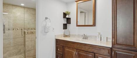 A modern bathroom with a glass shower enclosure, wooden vanity, and a large mirror.
