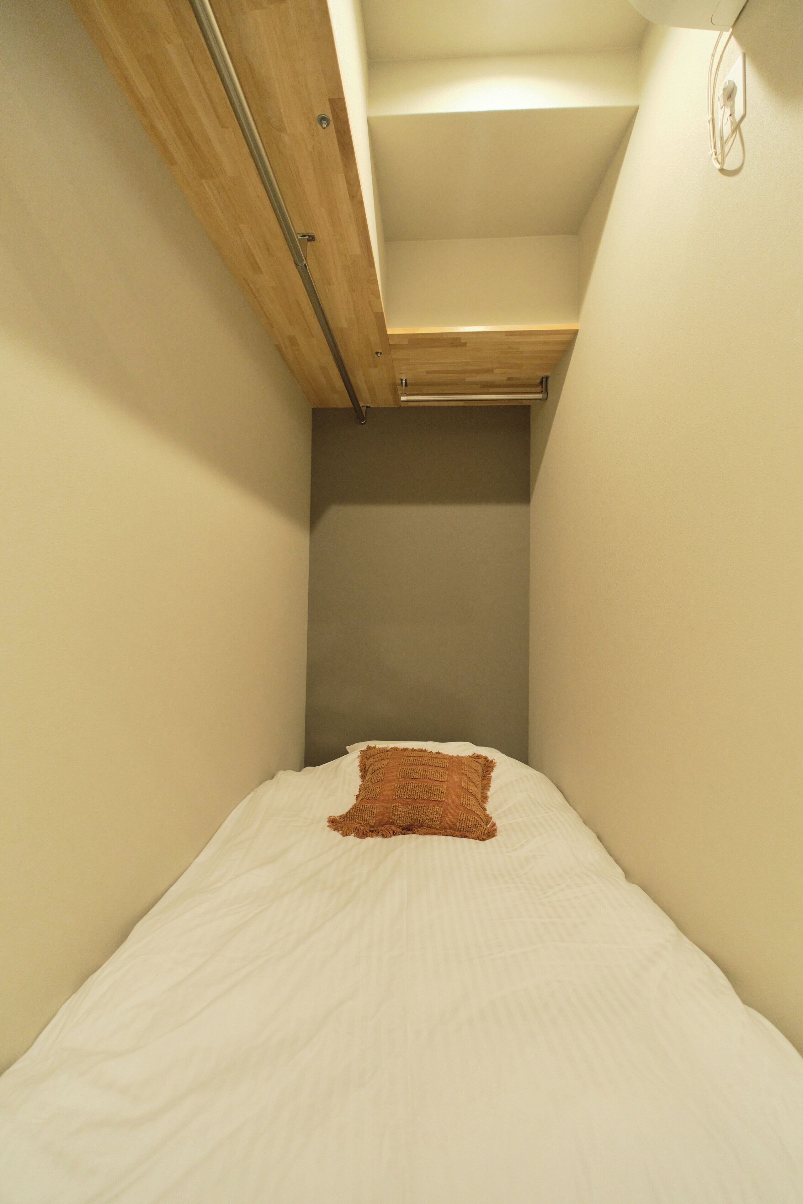 A narrow room with a bed, a wooden ceiling, and a wall-mounted light fixture.