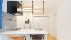 A modern kitchen with a white countertop, two bar stools, a built-in microwave, and a hanging light fixture. - Grand Maison Natsumesaka by Tranova (Tokyo)