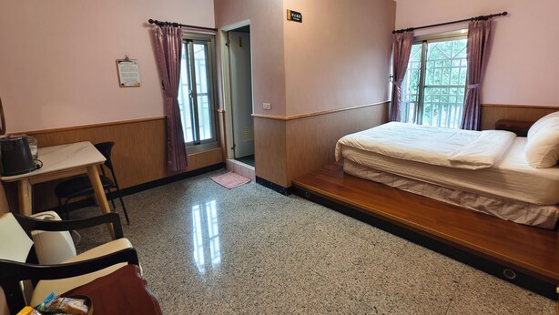 Ein Hotelzimmer mit Bett, Schreibtisch, Stuhl, einem kleinen Tisch mit Snacks und einem Fenster mit Vorhängen.