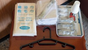 Ein Holztisch mit einem schwarzen Kleiderbügel, einer beigen Packung mit chinesischen Schriftzeichen sowie mehreren weißen Handtüchern und einer mit 'Beier' beschrifteten Flasche.