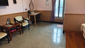 Ein Hotelzimmer mit Holztisch, Stühlen, Fernseher, Ventilator und einem Fenster mit Vorhängen.
