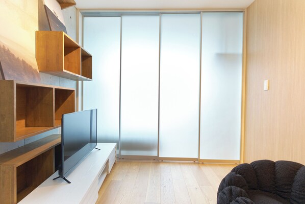 A modern living room with a flat-screen TV on a wooden stand, a dark sofa, and a sliding glass door leading to a balcony. - U Place Shimokitazawa (Tokyo)