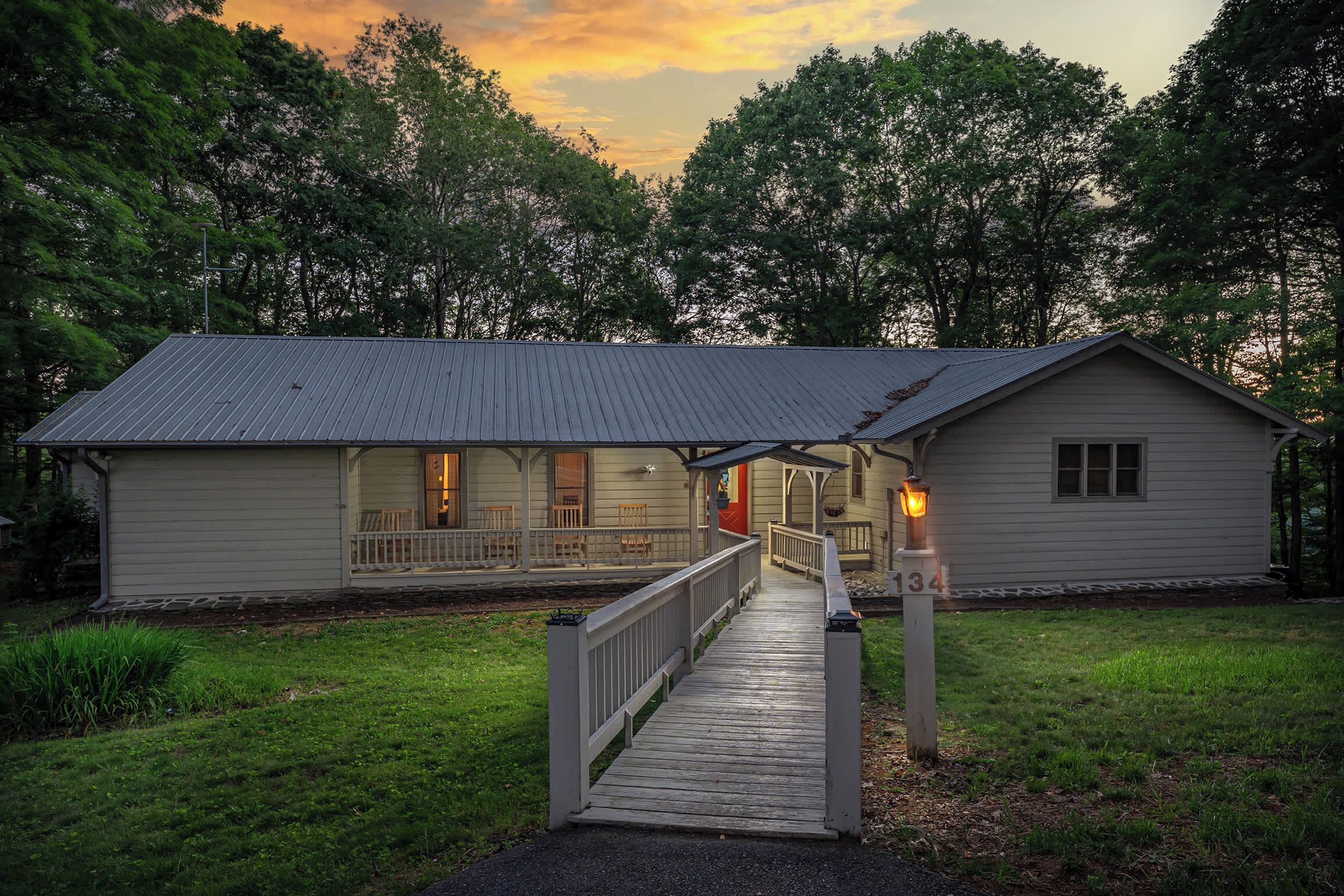 A two-story lodge with a porch and a covered deck, surrounded by trees.
