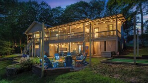A two-story wooden house with a covered deck, outdoor seating area, and a miniature golf course.