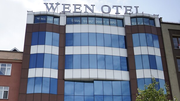 A modern hotel with a reflective glass facade, a prominent sign at the top, and a flagpole with a flag. - WEEN OTEL (Trabzon)