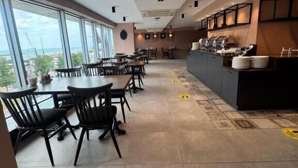 A spacious dining area with high ceilings, large windows offering a view of the outdoors, and a modern kitchen area with a buffet setup. - WEEN OTEL (Trabzon)