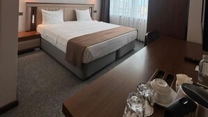 A hotel room with a large bed, a wooden desk, and a window with curtains. - WEEN OTEL (Trabzon)