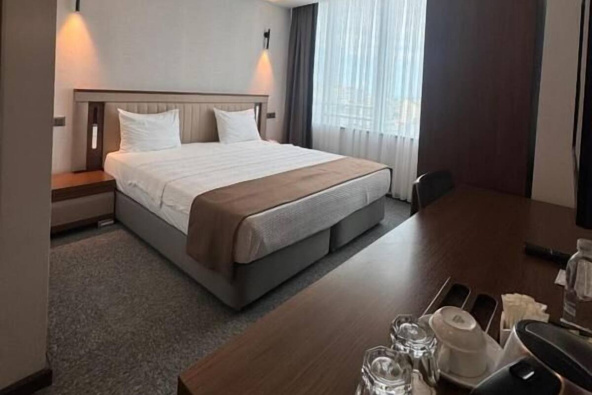 A hotel room with a large bed, a wooden desk, and a window with curtains.