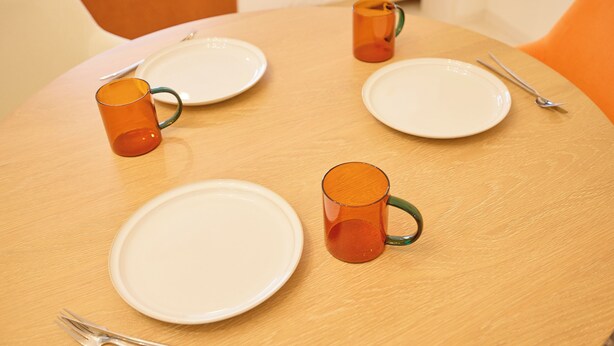 A round table with four white plates, two orange mugs, and two forks. - Cure Skytree by Tranova (Tokyo)