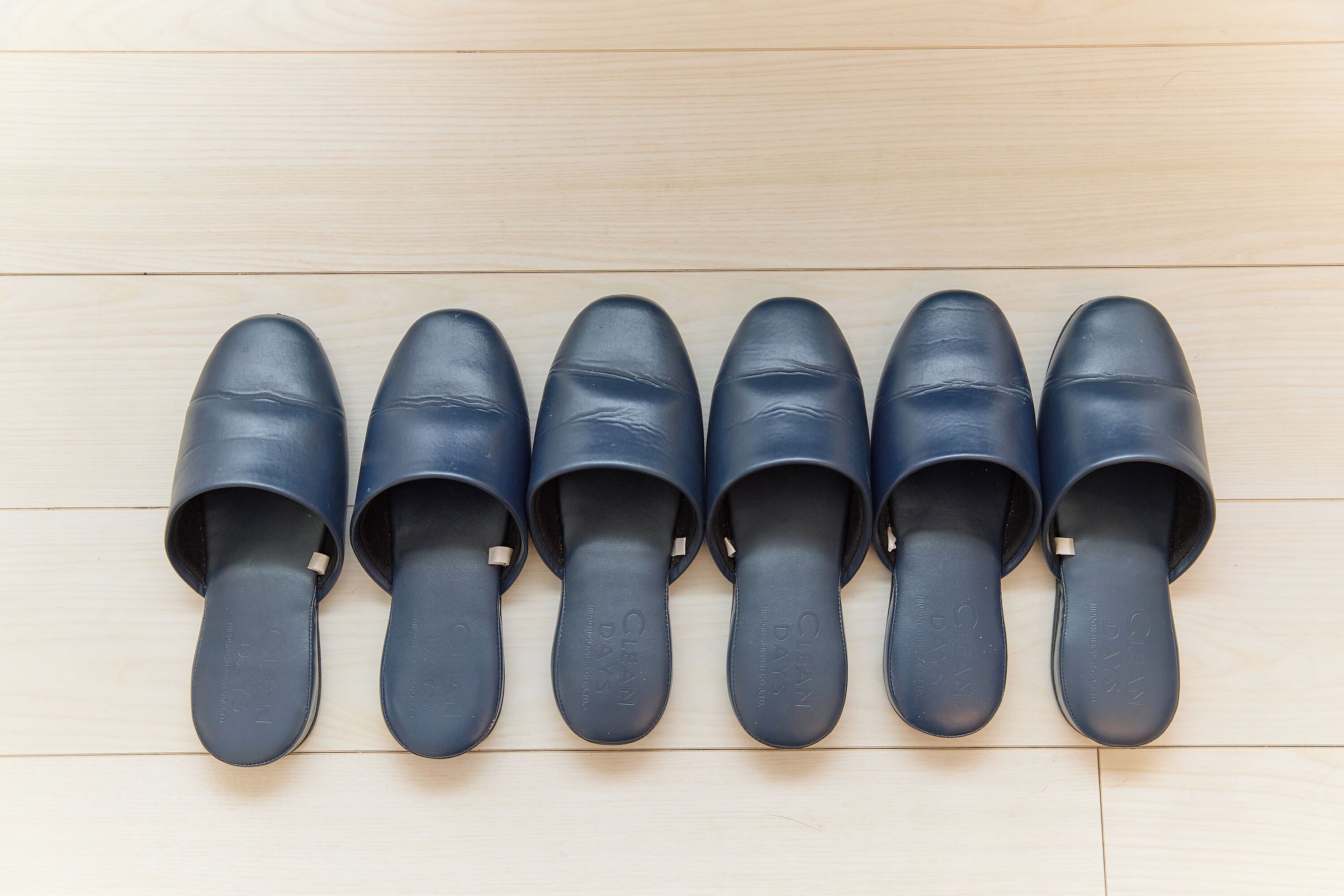A row of six black shoes on a wooden floor.