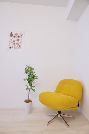 A yellow chair with a modern design, a white potted plant, and a wall with a botanical print. - Cure Skytree by Tranova (Tokyo)