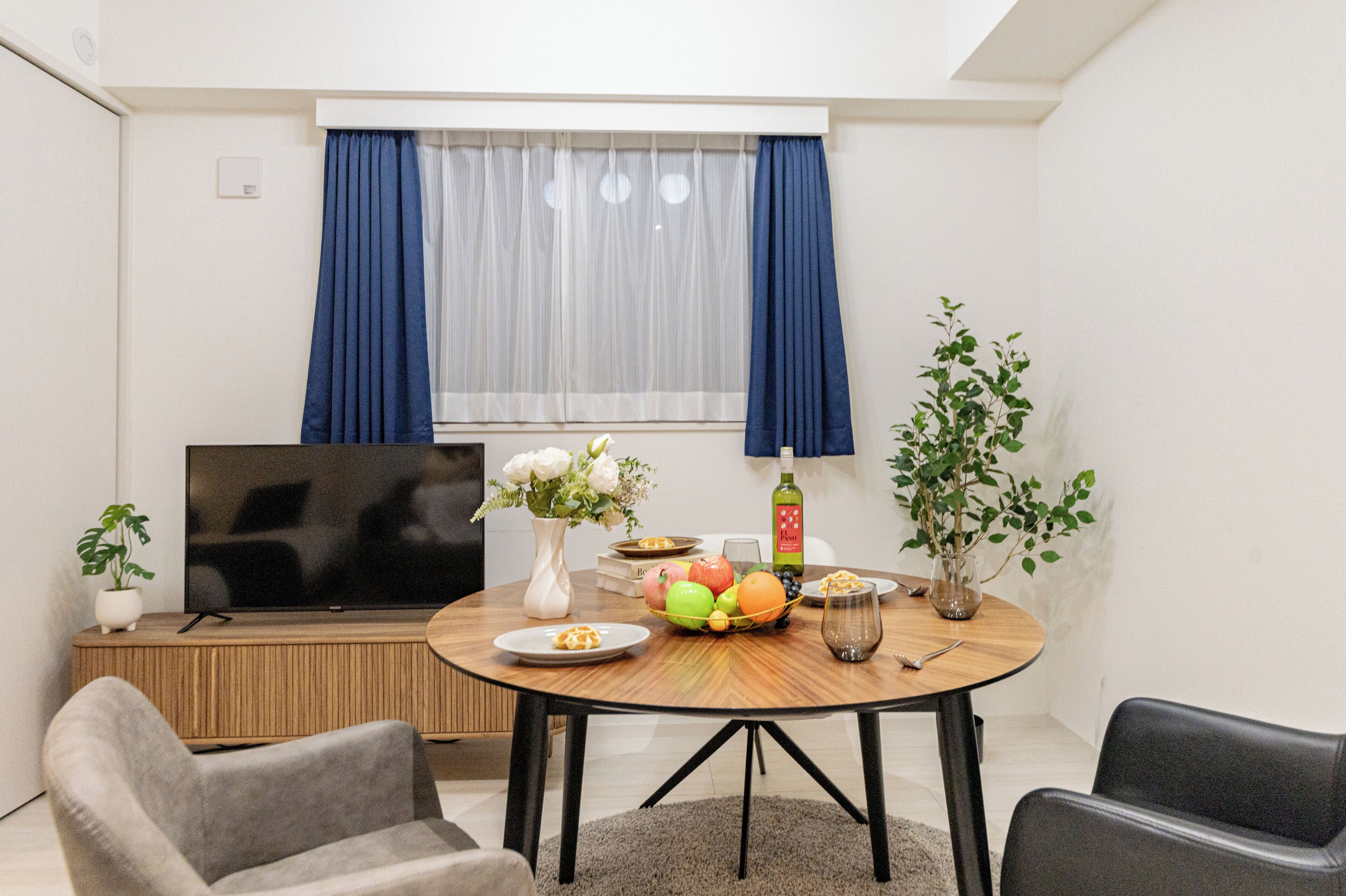 Un espacio habitable compacto con una mesa de comedor, sillas, un televisor de pantalla plana, una planta en maceta y una ventana con cortinas.