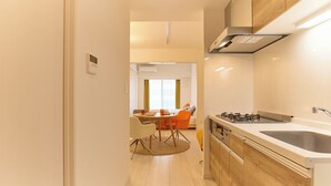 A modern kitchen with a central island, a dining area with orange chairs, and a view of a living room with a sofa and curtains. - Cure Skytree by Tranova (Tokyo)