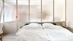 A bedroom with a large window, a bed with white bedding, and a green headboard. - Kings Square 3BR by Daniel&Jacob's (København)