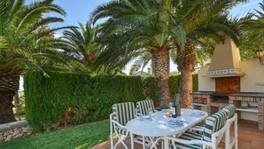 An outdoor patio with a round table, striped chairs, and a grill.