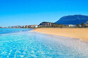 A beach with clear blue water, a sandy shore, and buildings in the background. - Alborada 4 pax - Denia, Costa Blanca (Denia)