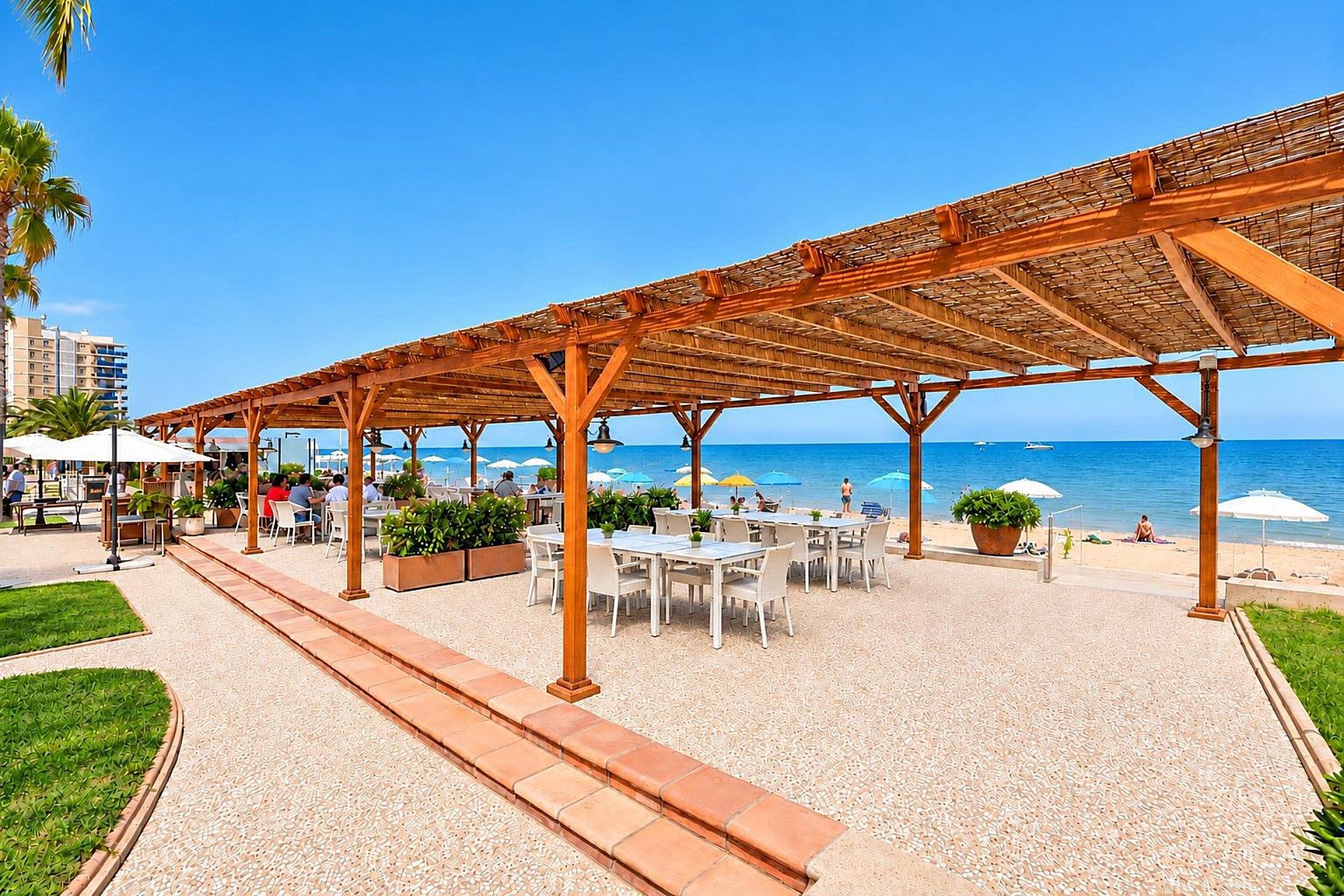Een buitenzitplaats met tafels en stoelen, een pergola en uitzicht op het strand en de oceaan.