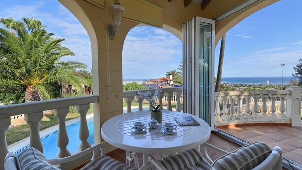 A balcony with a view of the sea, a pool, and outdoor seating.
