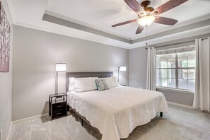 Une chambre à coucher avec un lit, des tables de chevet, un ventilateur de plafond et une fenêtre avec des rideaux.