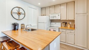 A kitchen with a wooden island, white cabinets, a microwave, a refrigerator, and a wall clock. - Stroll to The Village: Year-Round Family Getaway (Mammoth Lakes)