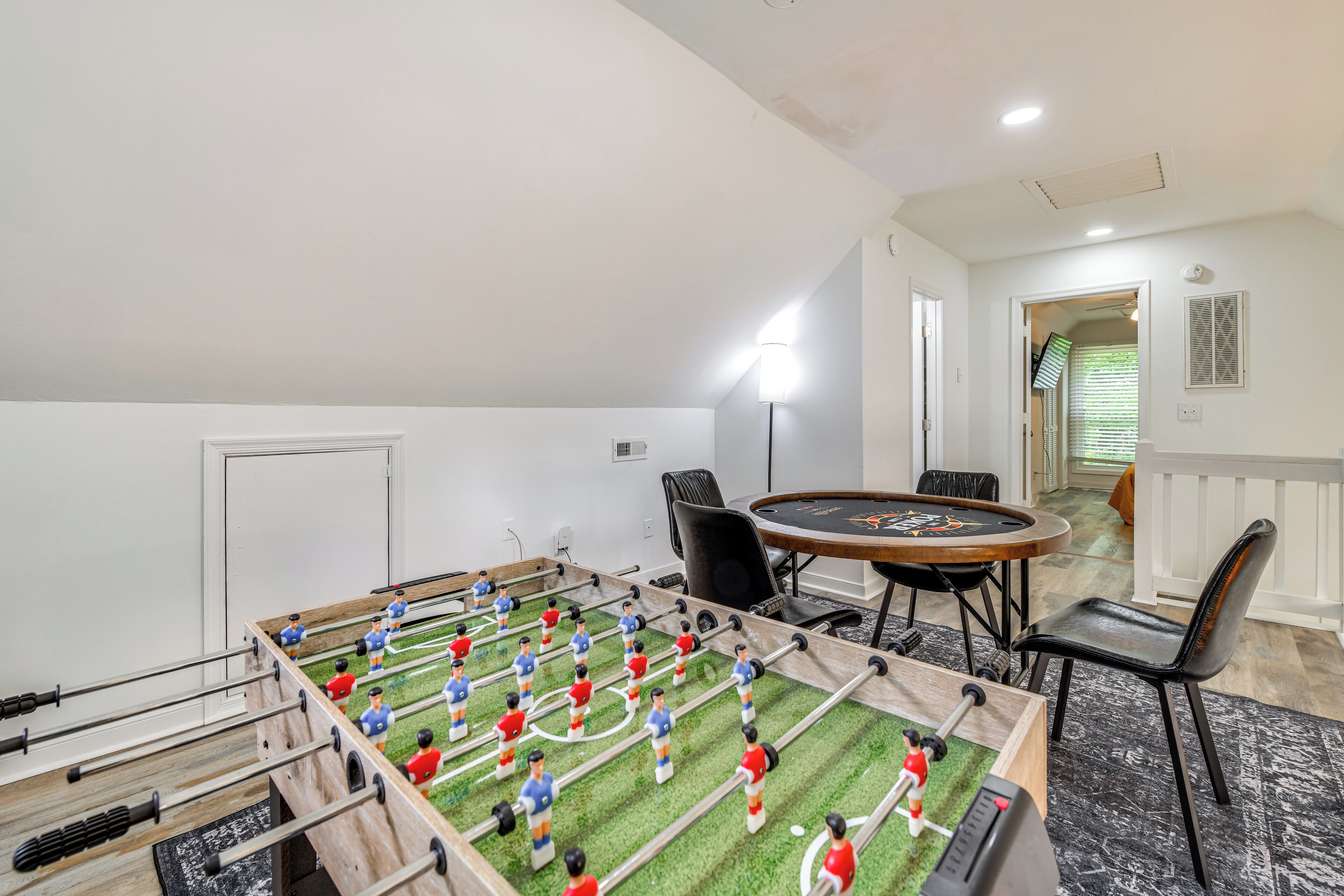 Um quarto com mesa de futebol, uma mesa redonda com cadeiras e uma escada que leva a outro espaço.