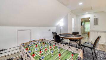 Um quarto com mesa de futebol, uma mesa redonda com cadeiras e uma escada que leva a outro espaço.
