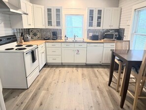 A kitchen with white cabinets, a stove, a microwave, and a wooden dining table.