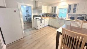 A modern kitchen with white cabinets, a wooden floor, and a dining area with a table and chairs. - Eastman Cottage Historic (St. Augustine)