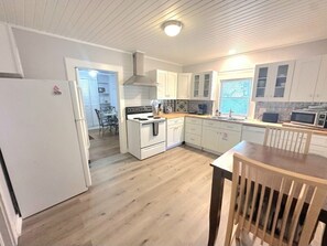A modern kitchen with white cabinets, a wooden floor, and a dining area with a table and chairs. - Eastman Cottage Historic (St. Augustine)