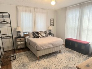 Un dormitorio con cama, mesitas de noche, un banco, un perchero y un tapete estampado.