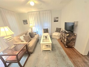 Una sala de estar con sofá, mesa de centro, televisor y mesita auxiliar.