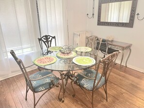 Un comedor con una mesa redonda de vidrio, seis sillas con cojines estampados, un espejo decorativo y piso de madera.