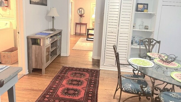 A dining area with a glass table and chairs, a red patterned rug, and a white door with shutters. - Eastman Cottage Historic (St. Augustine)