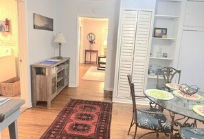 A dining area with a glass table and chairs, a red patterned rug, and a white door with shutters.