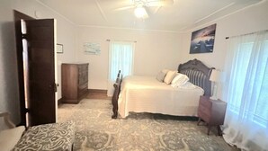 Ein Schlafzimmer mit einem Bett, einem Holzschrank, einem Nachttisch, einem Deckenventilator und einem Fenster mit Vorhängen.