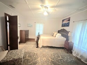 Ein Schlafzimmer mit einem Bett, einem Holzschrank, einem Nachttisch, einem Deckenventilator und einem Fenster mit Vorhängen.