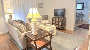 A living room with a sofa, two lamps, a glass coffee table, a TV, and a cabinet. - Eastman Cottage Historic (St. Augustine)