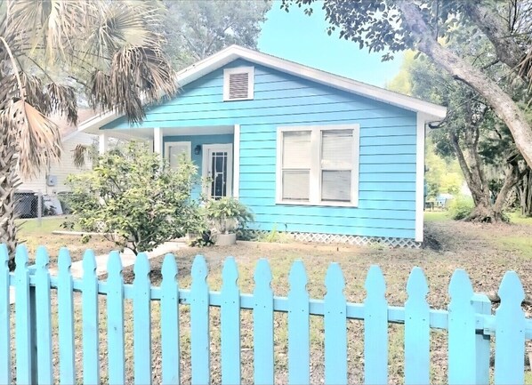 Una casa azul con valla de piquetes blancos, una puerta principal y un pequeño porche.