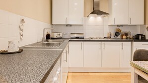 Een moderne keuken met witte kasten, een granieten aanrecht, een roestvrijstalen afzuigkap en een spoelbak.