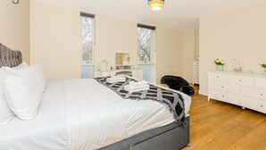 Een moderne slaapkamer met een groot bed, nachtkastjes, een dressoir en een zwart huisdierenbed.