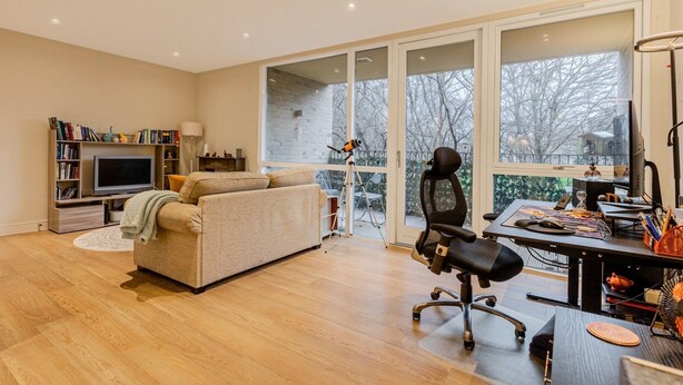 Een moderne woonkamer met een bank, televisie, boekenkast en een groot raam met uitzicht op bomen.