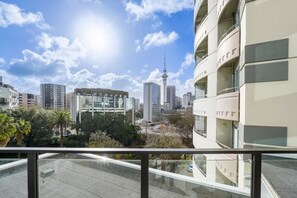 Un edificio moderno con balcones, cielo despejado y una torre distante.