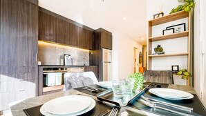 A modern kitchen with dark wood cabinets, a built-in oven, and a dining area with a glass table set for four. - Stylish 2-Bedroom Apartment in Central Auckland (Auckland)