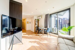Een moderne woonkamer met een flatscreen televisie, een eethoek met een tafel en stoelen, en een groot raam met uitzicht.