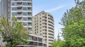 A modern multi-story building with balconies, a curved facade, and a tower structure in the background. - Stylish 2-Bedroom Apartment in Central Auckland (Auckland)