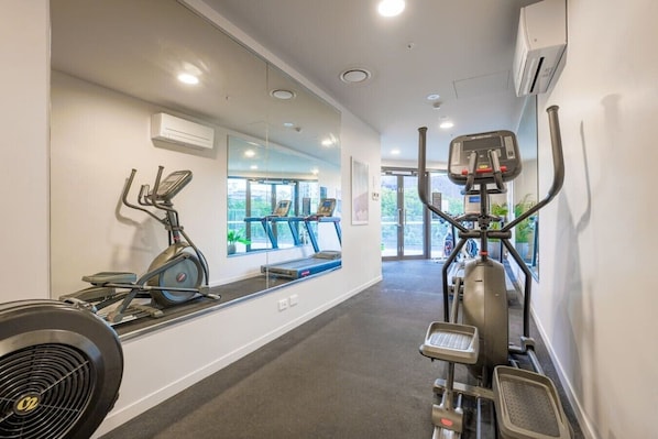 Uma academia com equipamentos de ginástica, um espelho grande e uma janela com vista para o exterior.