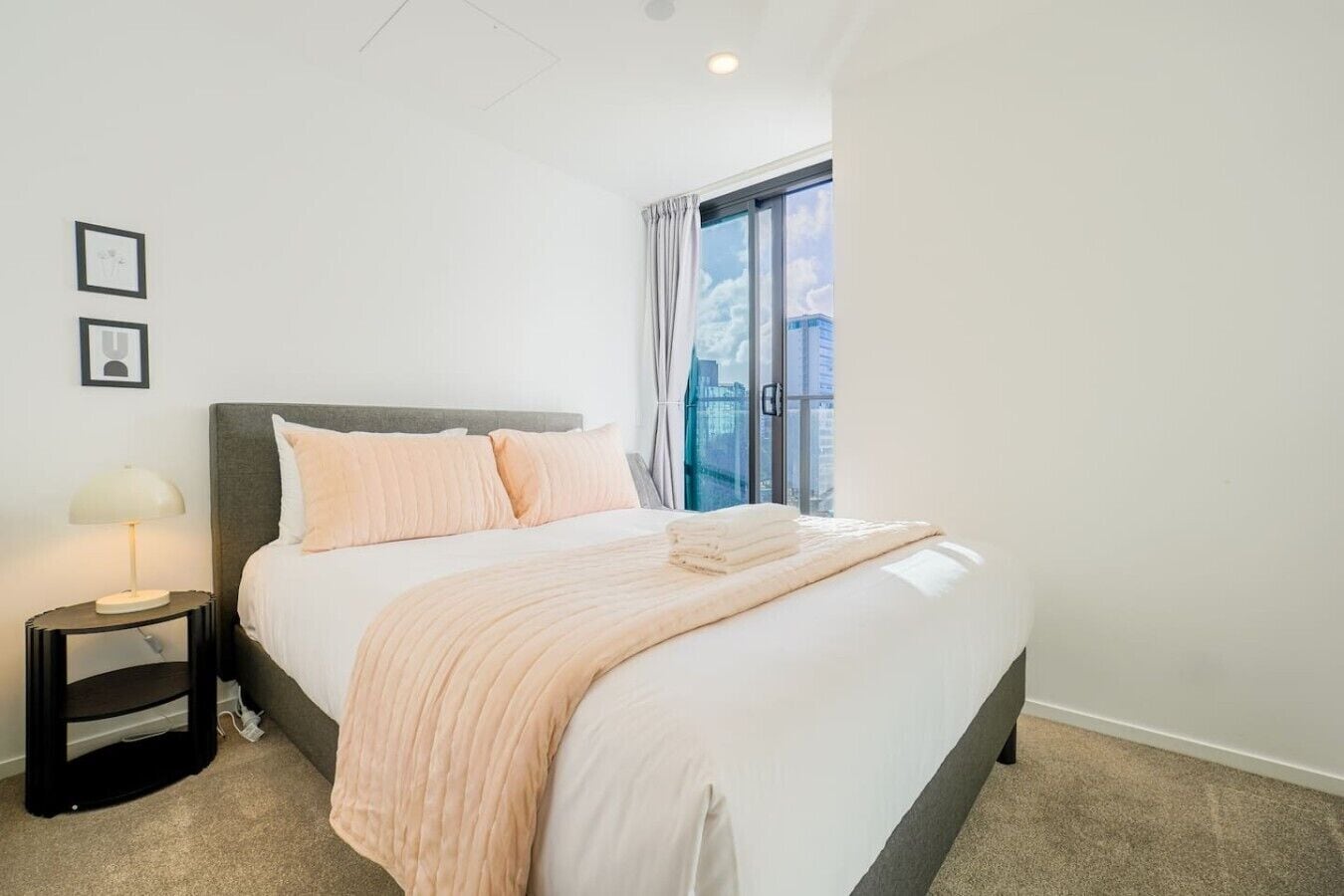 A neatly made bed with a headboard, a bedside lamp, and a window with curtains.